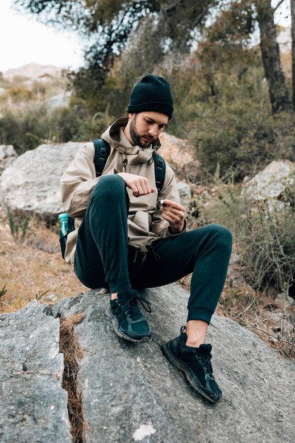 Un excursionista masculino sentado en la roca mirando la brújula de navegación