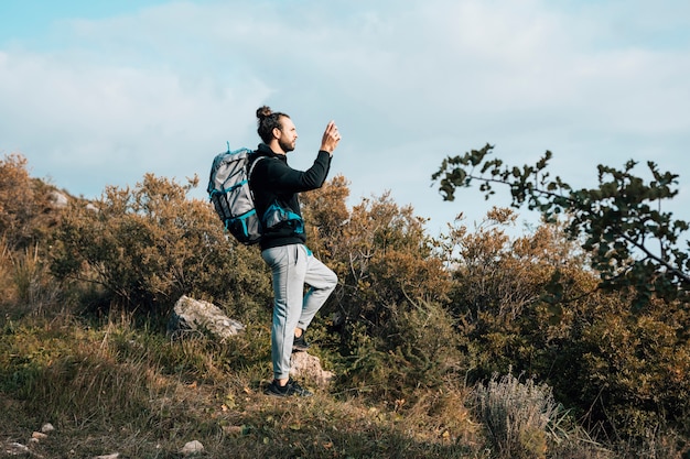 Un excursionista masculino con su mochila tomando fotos en la montaña