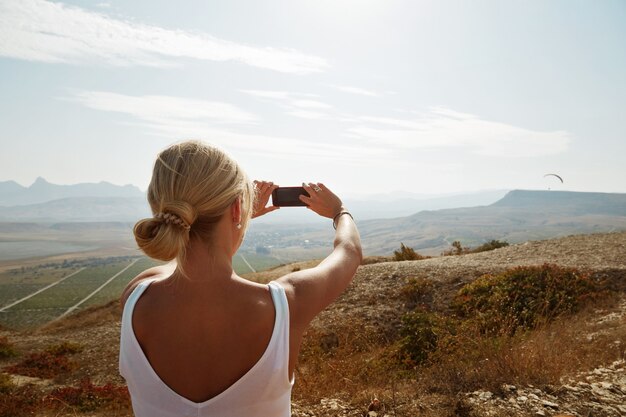 Excursionista de mujer tomando fotos con smartphone en el pico de la montaña