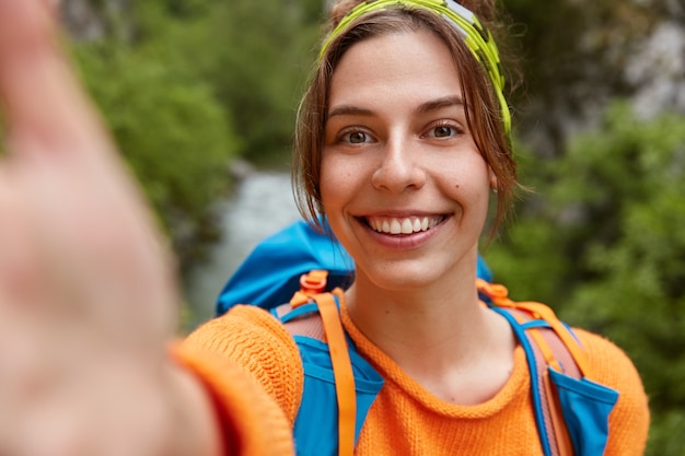 Foto gratuita excursionista mujer turista hace retrato selfie, sonríe a la cámara