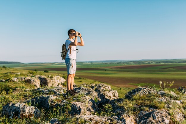 Excursionista de pie en la roca mirando a través de binoculares