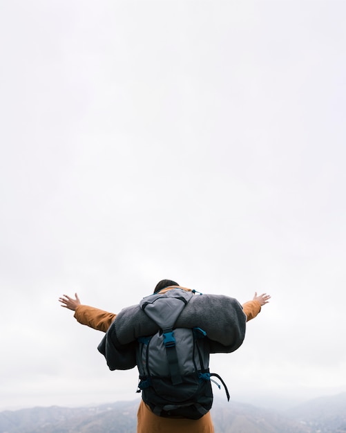 Foto gratuita un excursionista con su mochila estirándose las manos en la cima de la montaña