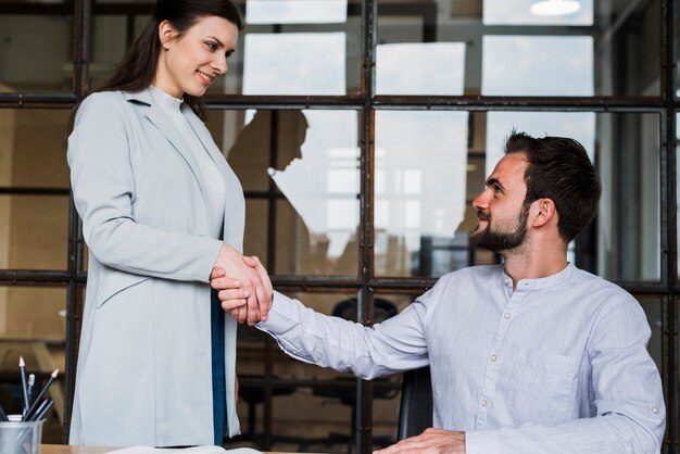 Exitosa empresaria joven estrechando la mano a un compañero de trabajo masculino