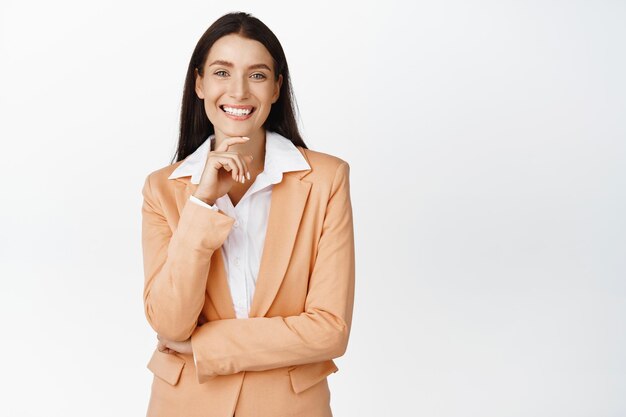 Exitosa mujer corporativa sonriendo luciendo feliz vistiendo traje de negocios de pie contra el fondo blanco.