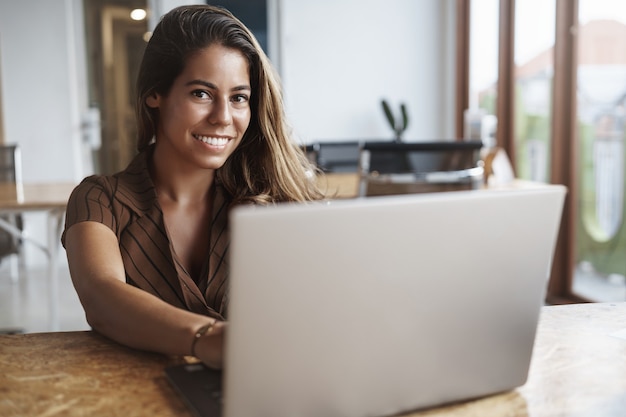 y exitosa mujer hispana sonriendo con laptop en cafe