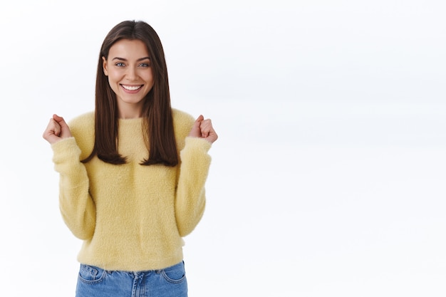 Exitosa mujer morena linda afortunada saltando de felicidad aprieta los puños y sonriendo feliz cámara como recompensa ganadora, logra la aprobación o premio, se convierte en campeona, triunfa