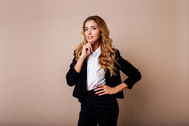 Exitosa mujer de negocios con sincera sonrisa y brazos cruzados en elegante traje en pared beige.