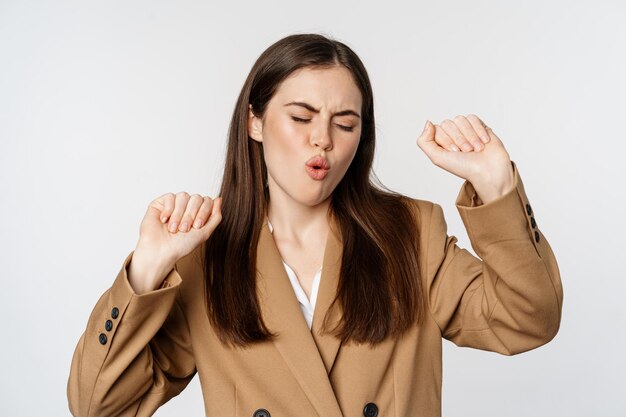 Exitosa mujer de negocios, vendedora bailando y divirtiéndose, usando traje de oficina, posando sobre fondo blanco.