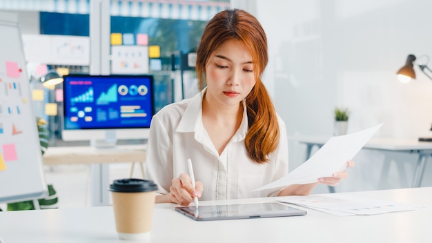 Exitoso ejecutivo de Asia joven empresaria elegante ropa casual dibujando, escribiendo y usando lápiz con tableta digital pensando en el proceso de trabajo de ideas de búsqueda de inspiración en la oficina en casa moderna.