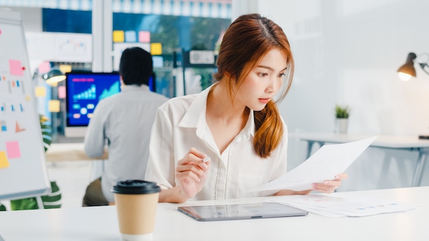 Exitoso ejecutivo de Asia joven empresaria elegante ropa casual dibujando, escribiendo y usando lápiz con tableta digital pensando en el proceso de trabajo de ideas de búsqueda de inspiración en la oficina en casa moderna.