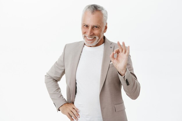Exitoso empresario masculino senior guapo mostrando gesto bien y sonriendo satisfecho