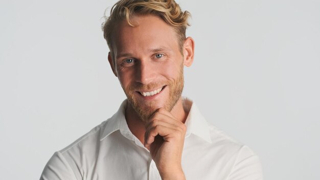 Exitoso hombre barbudo rubio sonriente felizmente posando en la cámara sobre fondo blanco Expresión feliz