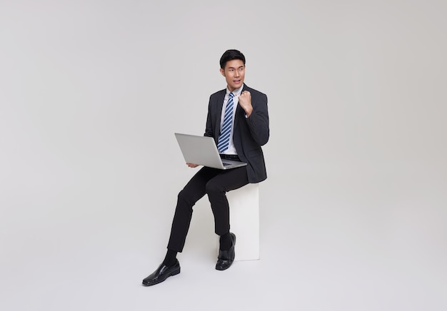 Exitoso hombre de negocios asiático que trabaja con una computadora portátil usando una computadora y sonriendo sentado