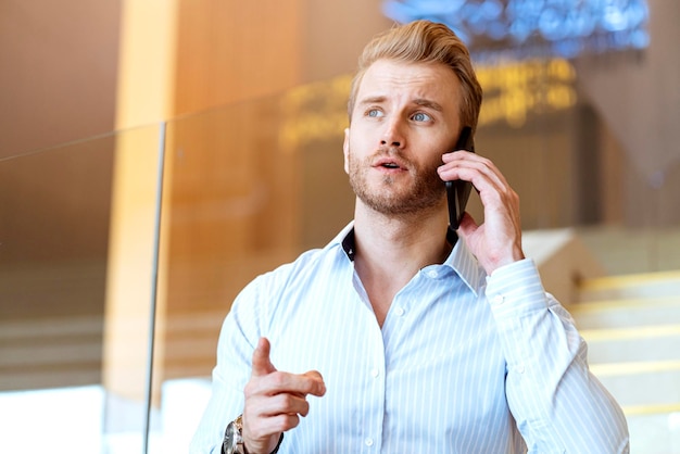 Foto gratuita el exitoso hombre de negocios caucásico inteligente que camina en la escalera hace que la comunicación con el teléfono inteligente se comunique con felicidad y un entusiasta fondo de oficina moderno