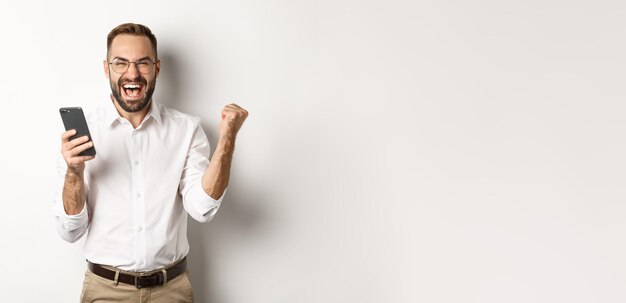 Foto gratuita exitoso hombre de negocios mirando feliz bomba de puño y regocijarse en ganar la lotería en línea de pie sobre w