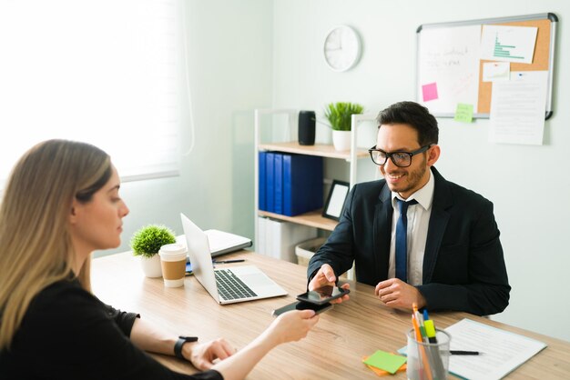 Exitoso profesional de negocios y jefe sonriendo mientras intercambia tarjetas digitales de negocios con una colega y cliente en su oficina corporativa