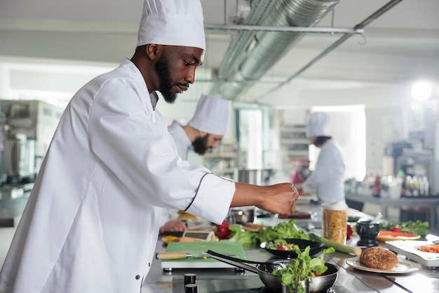 Experto en la industria alimentaria añadiendo hierbas verdes frescas para mejorar el sabor del plato. Experto en gastronomía con uniforme de cocina mientras prepara un delicioso plato gourmet para el servicio de cena en el restaurante.