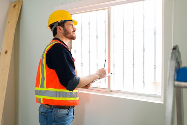 Experto en inspección enfocada con casco de seguridad comprobando la calidad de las ventanas y paredes en el sitio de construcción
