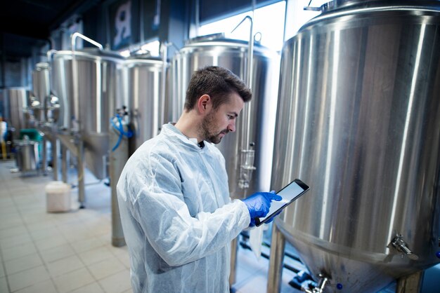 Experto en tecnología de pie en la planta de producción de alimentos y escribiendo en su tableta