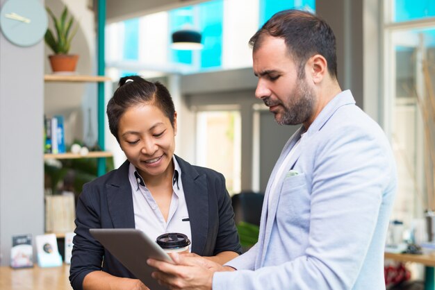 Expertos latinos y asiáticos positivos que sostienen café y tabletas.