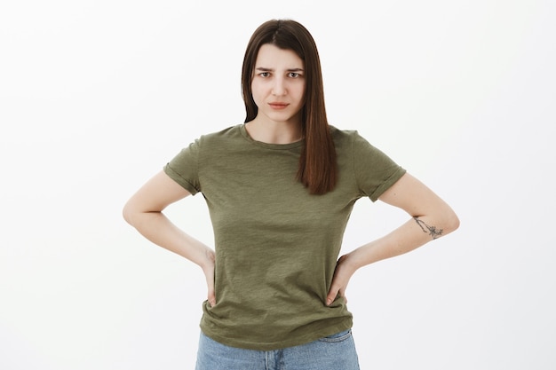 Foto gratuita explícate de inmediato. retrato de hermana mandona joven disgustada y enojada tomados de la mano con consternación en la cintura frunciendo el ceño y mirando con mirada de juicio, decepcionada por la pared gris