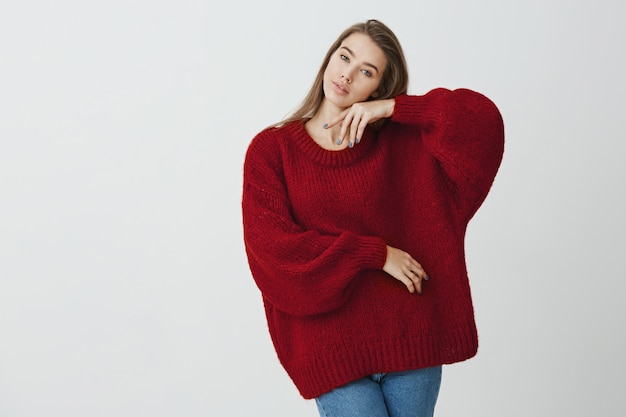 Explora tu sensualidad. Foto de estudio de increíble delgada mujer europea inclinando la cabeza y tiernamente tocando la cara con la mano, posando para comerciales en suéter de invierno.