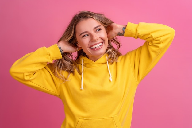 Expresión de la cara linda de la mujer bastante rubia joven que presenta en sudadera con capucha amarilla en rosa