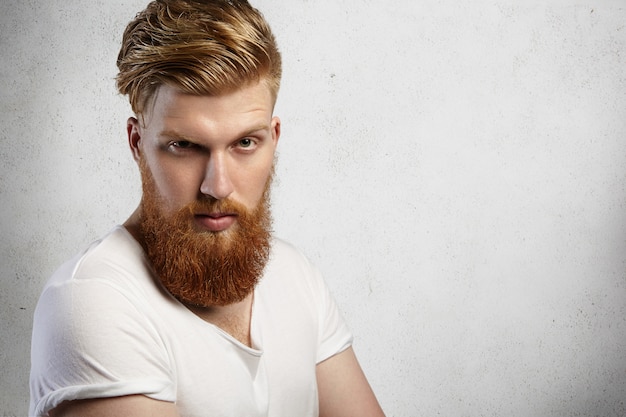 Foto gratuita expresiones y emociones del rostro humano. foto de cabeza de modelo joven con barba espesa posando con mirada enojada y antipática.