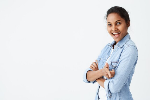 Expresiones faciales humanas positivas, emociones, sentimientos, reacción y actitud. Atractiva mujer afroamericana con bollo de pelo, sonriendo con teet. mirarte y señalarte con el dedo índice