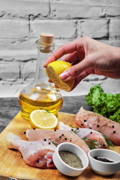 Exprima con la mano limón fresco en un plato de carnes de pollo crudas con un montón de verduras.