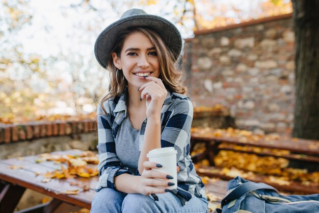 Extasiada mujer blanca en camisa casual sosteniendo una taza de té en el desenfoque de fondo de otoño