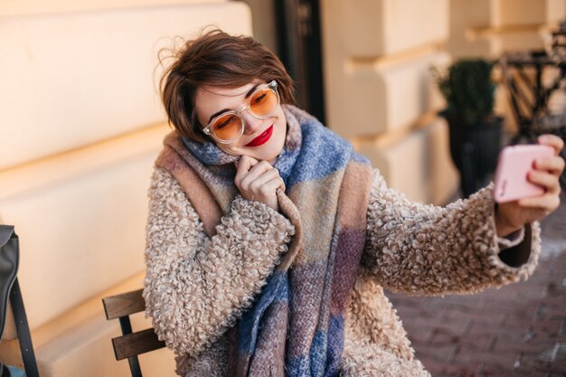 Extasiada mujer de pelo corto tomando selfie en la calle