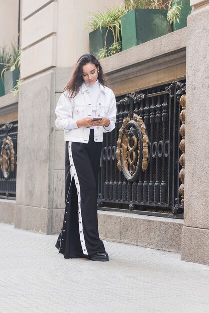 Exterior derecho de moda de la mujer joven usando el teléfono móvil