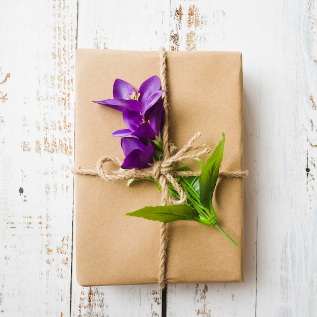 Falsas flores púrpuras y caja de regalo atadas con una cuerda sobre fondo de madera
