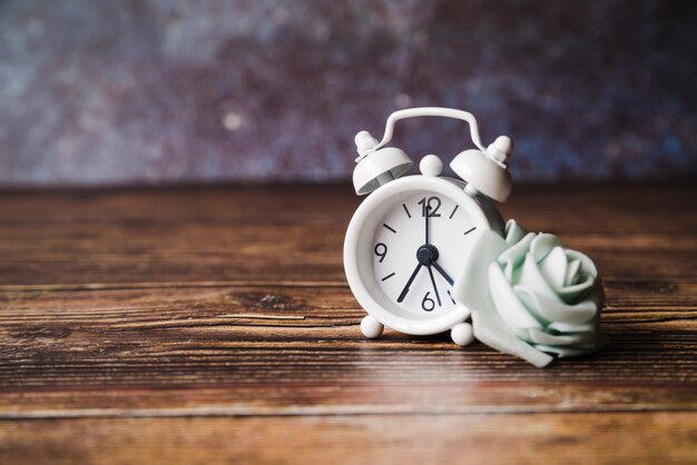 Falso rosa blanca con reloj despertador sobre fondo de madera