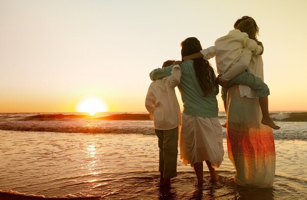 Familia abrazándose mientras está de pie en la playa rodeada por el mar durante la puesta de sol
