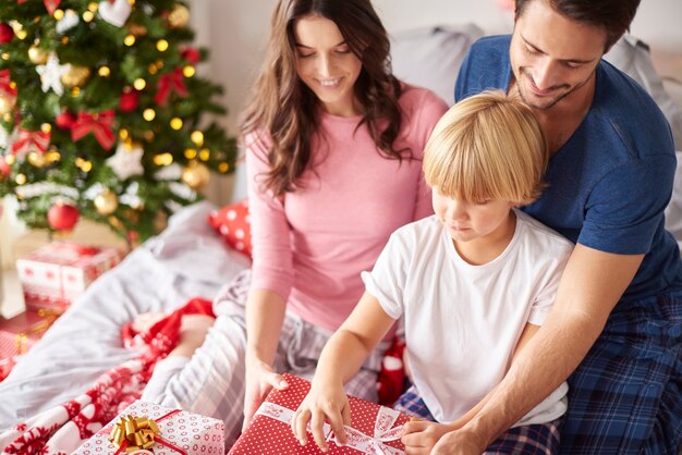 Familia abriendo regalos de Navidad en la cama