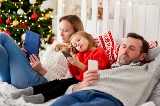 Familia aburrida con teléfono móvil en la cama en Navidad