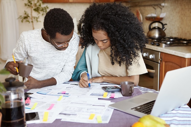 Familia africana joven que tiene problemas de deuda, no puede pagar el gas y la electricidad, administrar las finanzas, sentarse a la mesa de la cocina con papeles, calcular facturas, tratar de reducir sus gastos domésticos