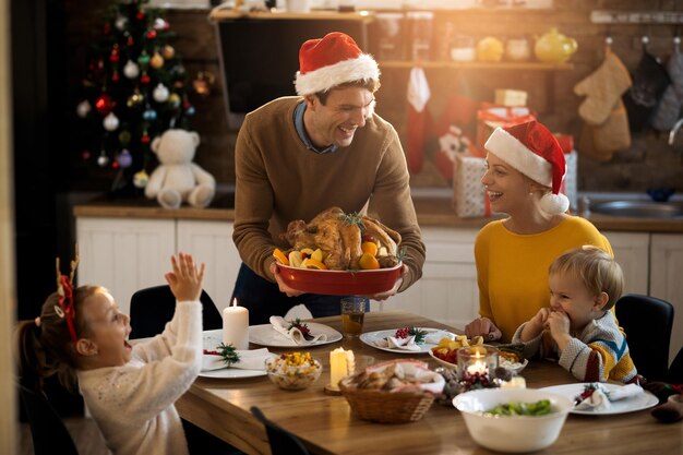 Familia alegre con pavo relleno para almorzar el día de Navidad en casa