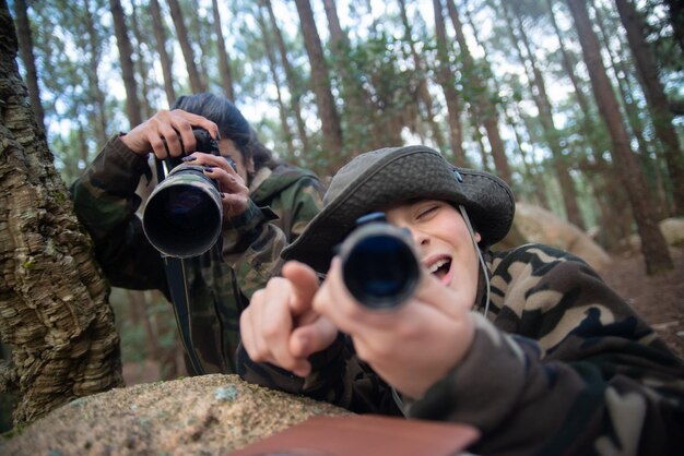 Familia alegre tomando fotos en el bosque. Madre e hijo dirigiendo la lente a la cámara. Crianza, familia, concepto de ocio.