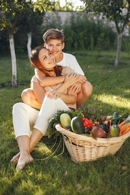 Familia alegre con verduras orgánicas en el jardín. Vegetales orgánicos mixtos en canasta de mimbre. Madre con hijo en un patio trasero.