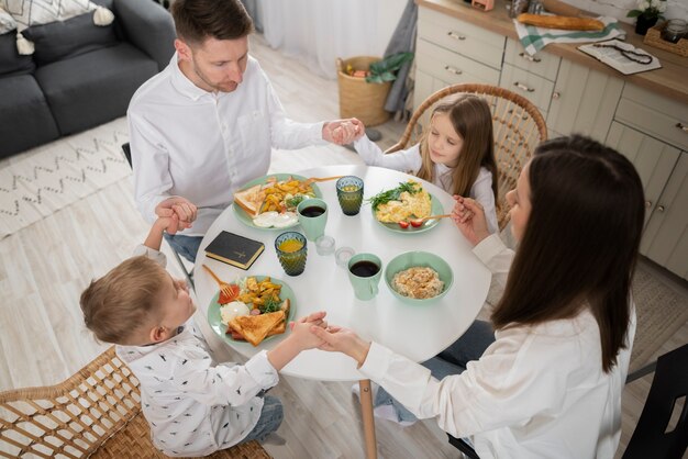 Familia de alto ángulo rezando en la mesa