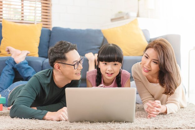 Familia asiática feliz usando la computadora portátil junto en el sofá en la sala de estar de casa.