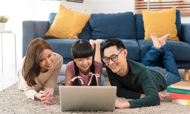 Familia asiática feliz usando computadora portátil juntos en casa en la sala de estar