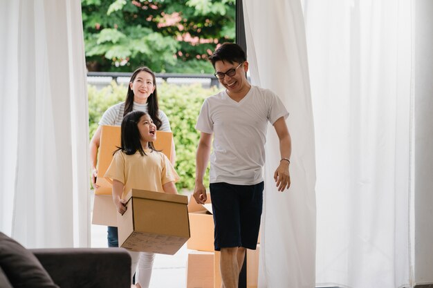 Familia asiática joven feliz compró casa nueva. Los japoneses mamá, papá y niño sonriendo felices sostienen cajas de cartón para mover objetos caminando en una gran casa moderna. Nueva vivienda inmobiliaria, préstamo e hipoteca.