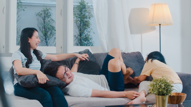 La familia asiática joven feliz juega junto en el sofá en casa. China madre padre e hija hijo disfrutando feliz relajarse pasar tiempo juntos en la moderna sala de estar en la noche.