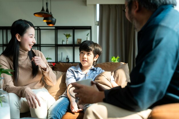 Familia asiática sentarse relajarse conversación positiva con hijo felicidad sonrisa niño casual hablando con su padreFeliz familia asiática disfrutar de vacaciones juntos en el sofá hogar dulce hogar sala de estar