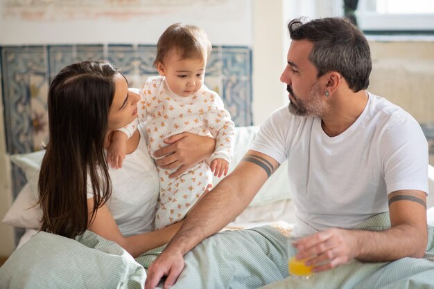 Familia con bebé sentados juntos en la cama por la mañana