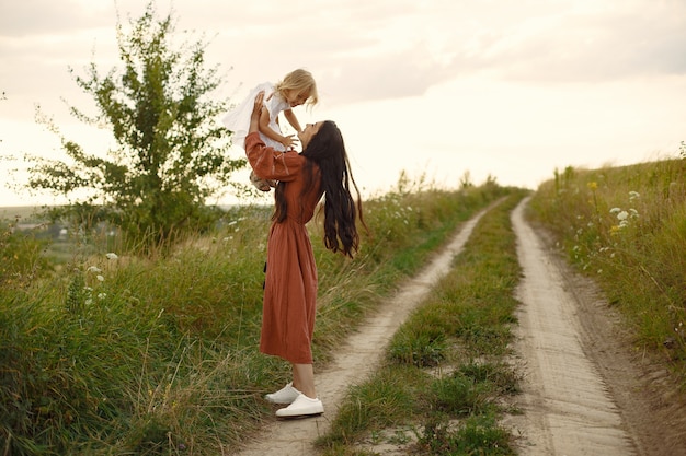 Familia en un campo de verano. Madre con un vestido marrón. Pequeña niña bonita.